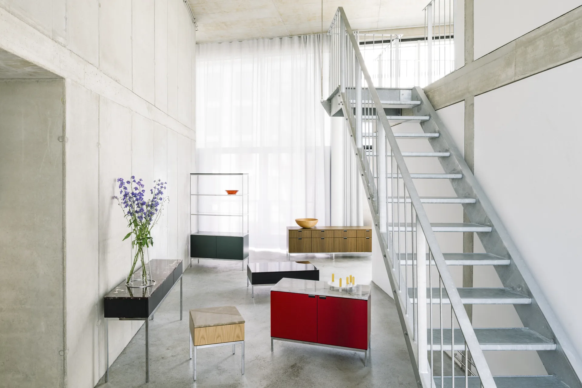 Knoll Chermayeff Storage: red credenza, black console and open shelving in a concrete loft with a steel staircase