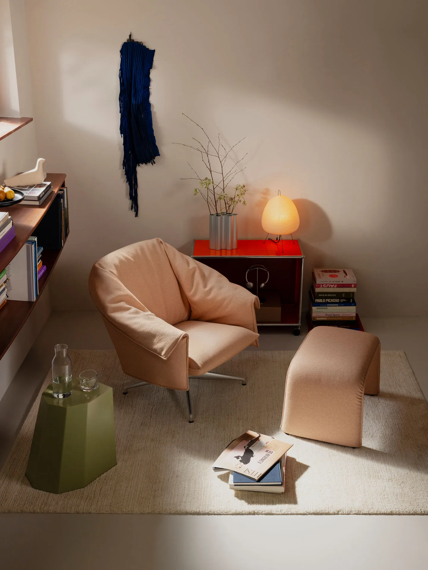 Vitra Bascule lounge chair in peach fabric with ottoman beside a sideboard and lamp